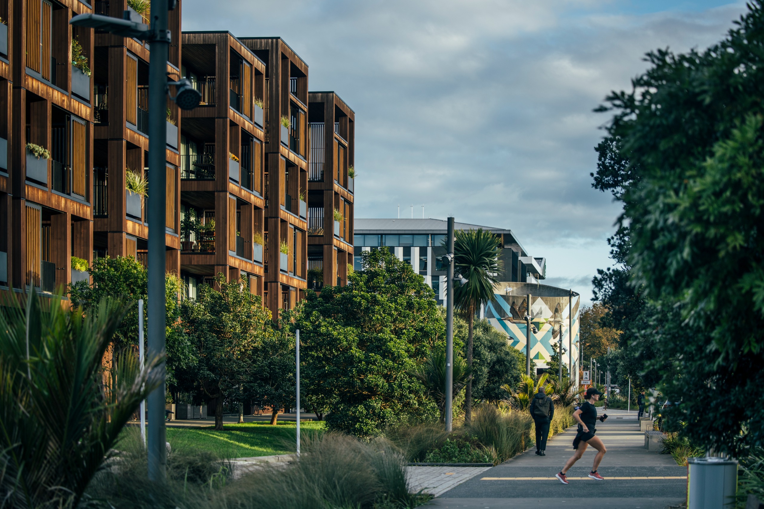 A block of apartments with green space in front made up of trees and pathways.